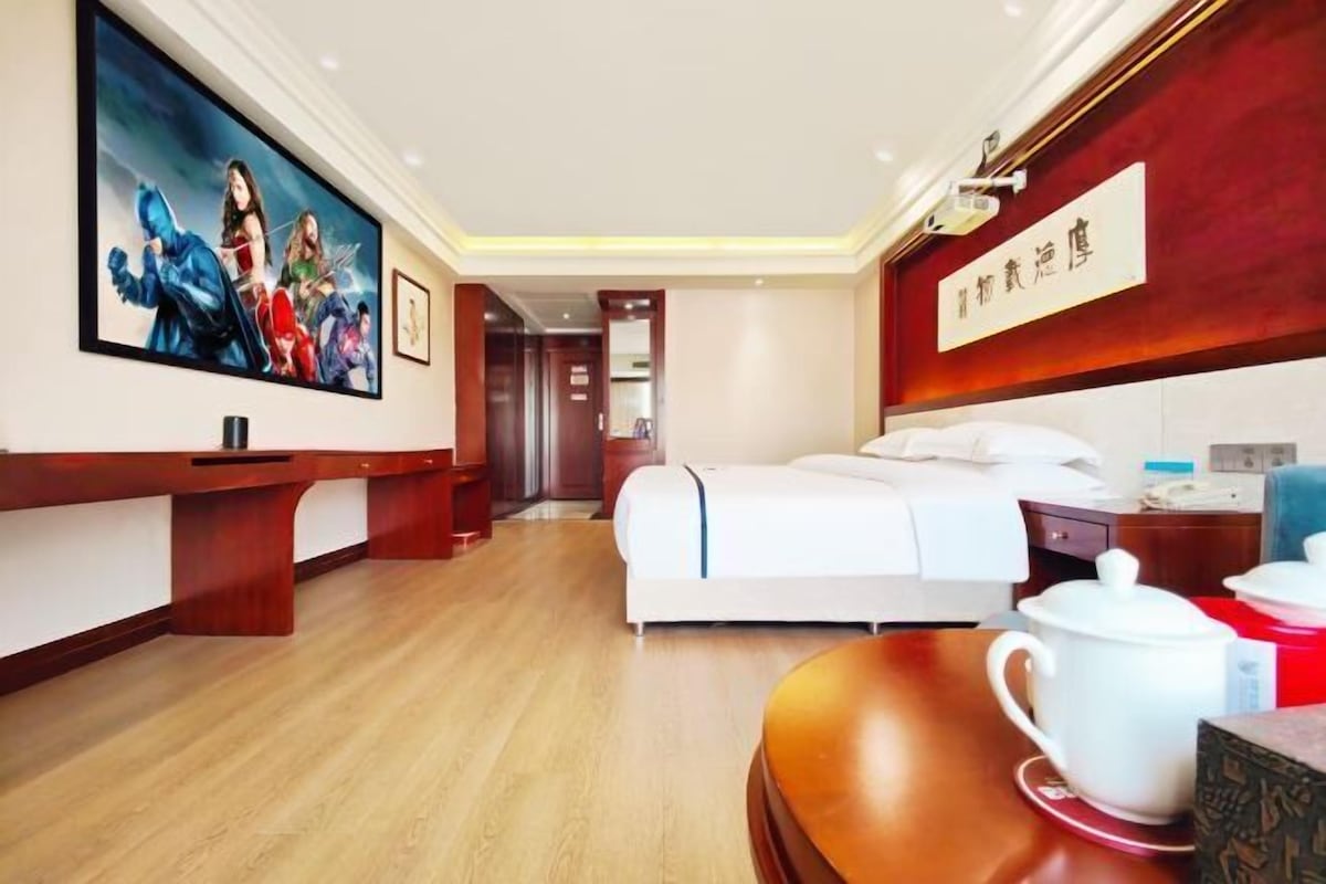 A hotel room with a bed, a desk, a painting, and a sign on the wall.