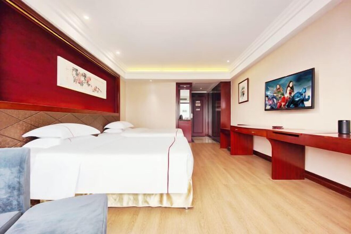 A hotel room with a bed, bedside tables, a desk, and artwork on the walls.