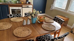 Ein Essbereich mit einem Holztisch, gewebten Tischsets, einer Obstschale und stuhlartigen Sitzgelegenheiten mit Muster.