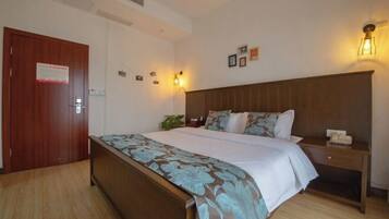 A hotel room with a wooden bed, a nightstand, a wall-mounted lamp, and a door with a sign.