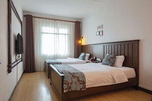 Una habitación de hotel con dos camas, televisión, ventana con cortinas y una mesita de noche.