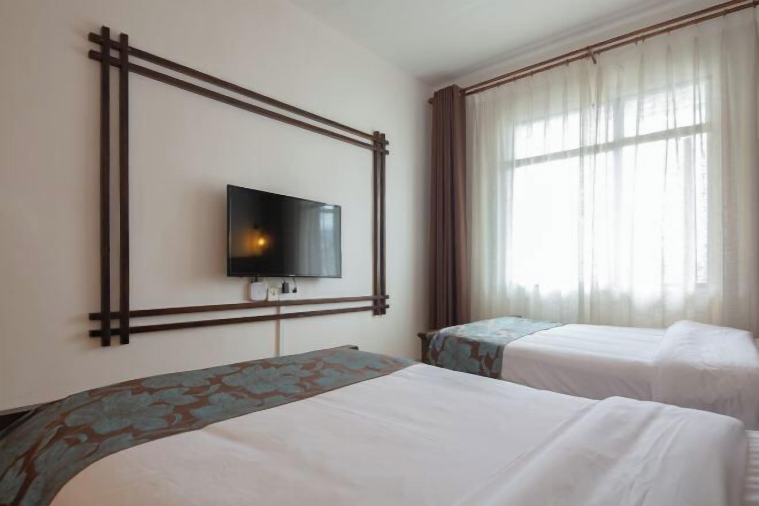 Een hotelkamer met twee bedden, een aan de muur bevestigde televisie en een raam met gordijnen.