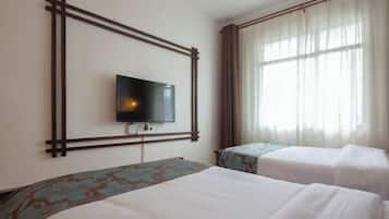 Een hotelkamer met twee bedden, een aan de muur bevestigde televisie en een raam met gordijnen.