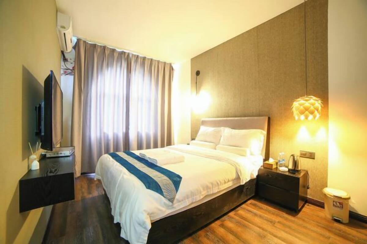 A hotel room with a bed, bedside tables, a television, and a wall-mounted heater.