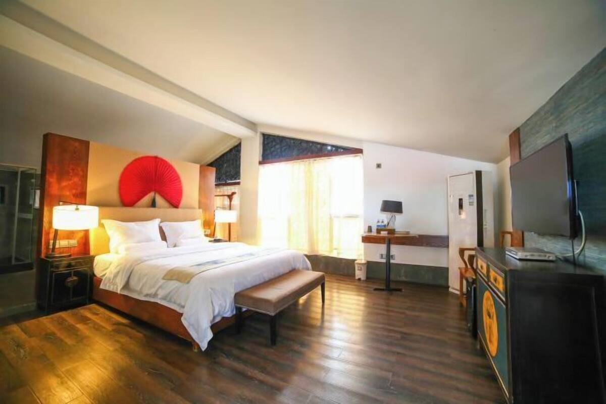 A bedroom with a bed, bedside table, lamp, bench, and a dresser.