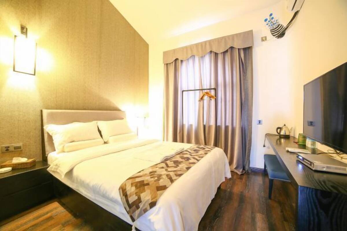 A hotel room with a bed, bedside table, and a desk with a chair.