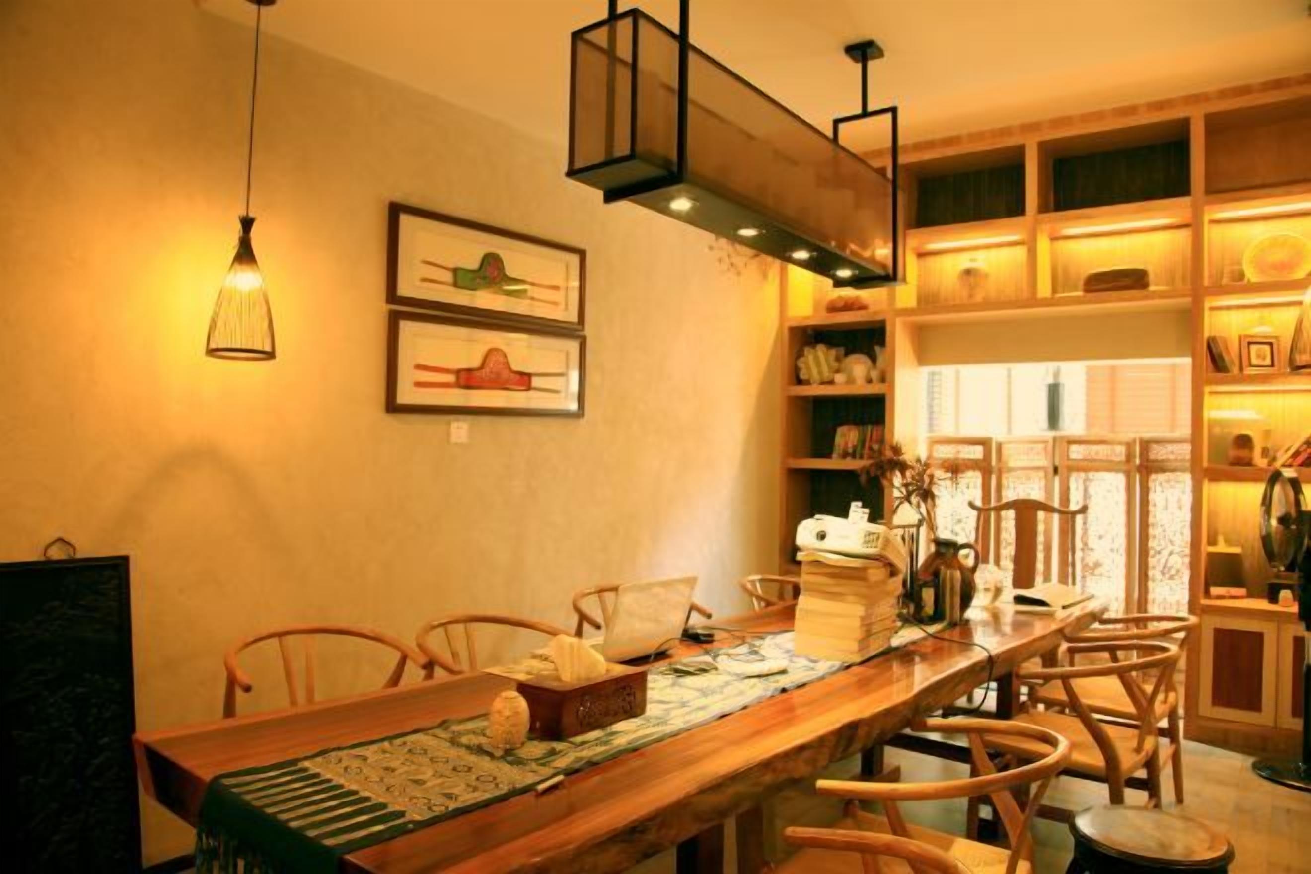 A dining area with a long wooden table, chairs, hanging lights, and shelves with books and decorative items.
