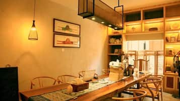 A dining area with a long wooden table, chairs, hanging lights, and shelves with books and decorative items.