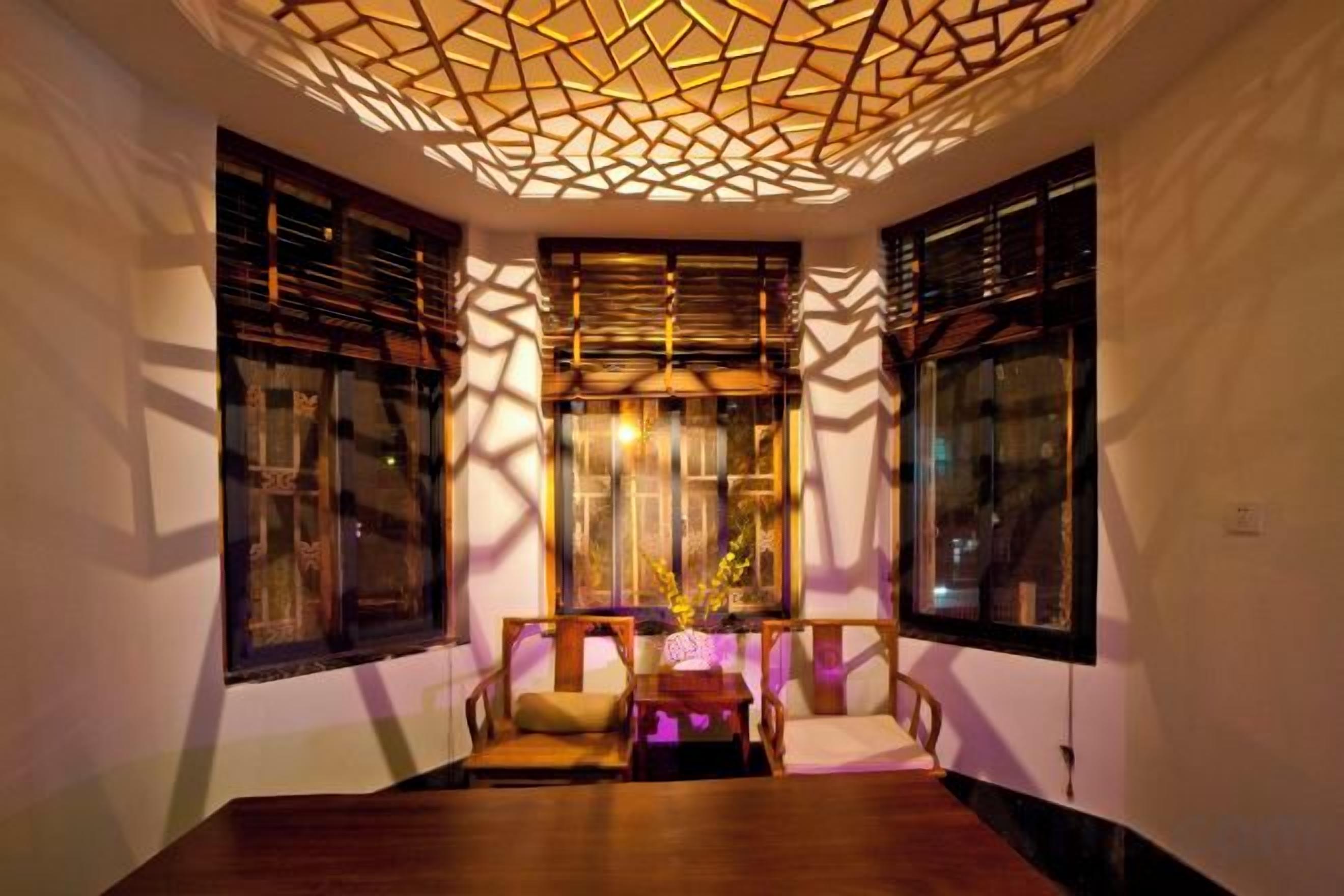 A room with a wooden table, two chairs, a decorative ceiling, and windows with wooden shutters.