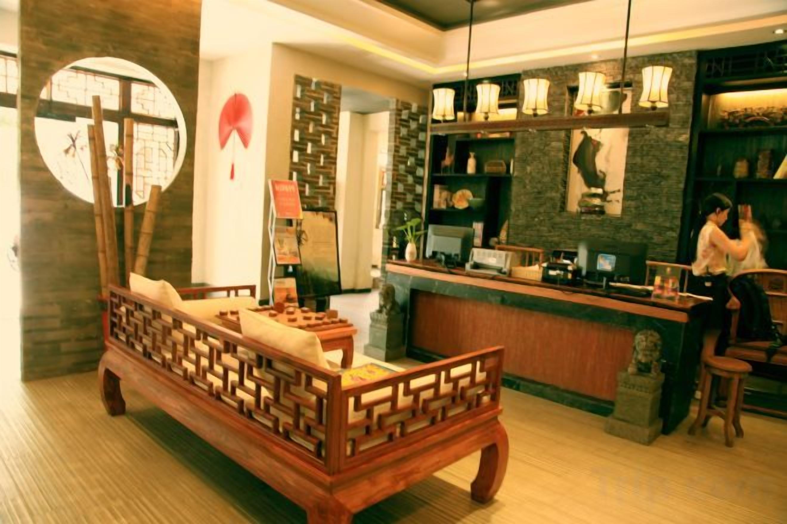 A traditional wooden bed with a cushion, a reception desk, and a wall with a circular mirror and decorative items.