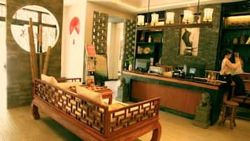 A traditional wooden bed with a cushion, a reception desk, and a wall with a circular mirror and decorative items.