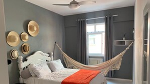 A bedroom with a bed, a hammock, and a window with curtains.