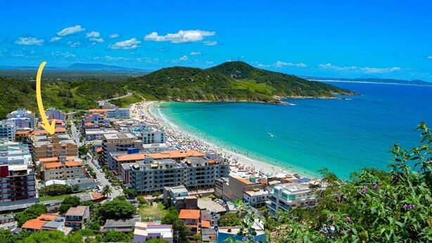 A coastal town with a beach, buildings, and a hilly landscape.