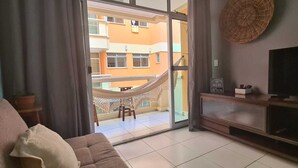 A living room with a sofa, a TV, a wicker wall hanging, and a view of a building through a glass door.