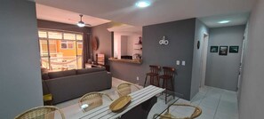 Uma sala de estar moderna com sofá, mesa de jantar e cadeiras. Há uma varanda com vista para o exterior.