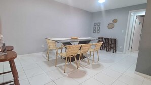 A dining area with a glass-top table, wicker chairs, and a bowl on the table. There are two wooden chairs and a small table in the background.