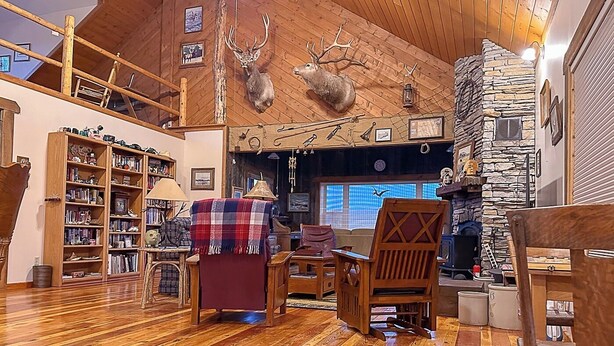 L’intérieur chaleureux d’un chalet avec un plancher en bois, une cheminée en pierre, une bibliothèque et des têtes de cerf accrochées au mur.