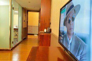 Un pasillo de hotel con suelo de madera, un mostrador de recepción y una pantalla de televisión que muestra a una persona con traje.