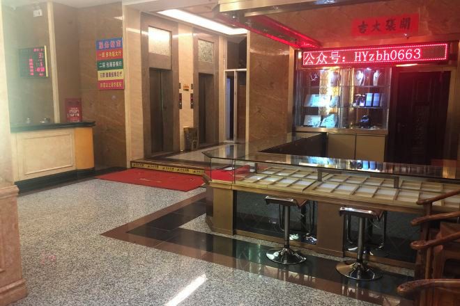 Un vestíbulo de hotel con una mesa de recepción, una vitrina de cristal y un letrero de neón rojo.