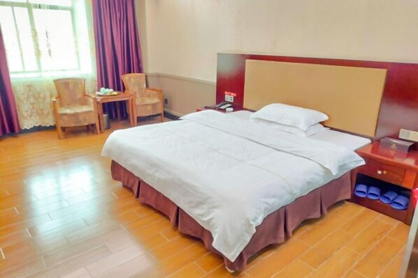 A hotel room with a bed, a desk, chairs, and a nightstand. - Huayang Hotel (Puning)