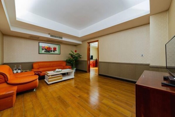 A spacious room with a wooden floor, a sofa, a coffee table, and a desk. - Huayang Hotel (Puning)