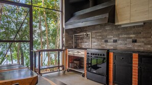 A kitchen with a brick backsplash, a large window overlooking greenery, and a built-in oven. - Bacalar Casa Relaxo on the Lagoon with Private Dock (Buenavista Bacalar)