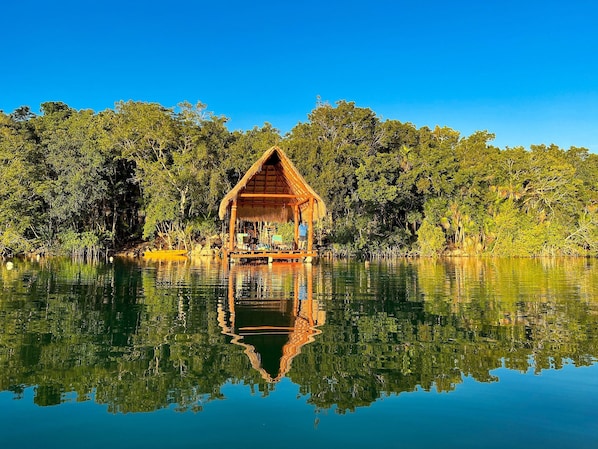 A thatched-roof hut with a view of a calm lake and dense forest.