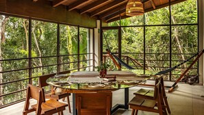 A dining area with a glass table, wooden chairs, and a view of lush greenery through large windows. - Bacalar Casa Relaxo on the Lagoon with Private Dock (Buenavista Bacalar)