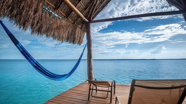 A wooden deck with a hammock and two chairs overlooking a clear blue sea. - Bacalar Casa Relaxo on the Lagoon with Private Dock (Buenavista Bacalar)