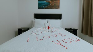 A neatly made bed with a towel and red crosses arranged on the bedspread, a painting of a coastal scene on the wall, and a window with curtains. - Havana jacó (Jacó)