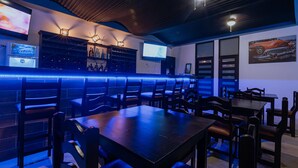 A bar area with wooden furniture, a TV screen, and a blue neon light. - Havana jacó (Jacó)