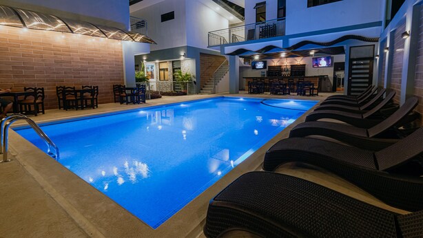 A modern indoor pool area with a clear blue pool, lounge chairs, and a bar area with seating. - Havana jacó (Jacó)