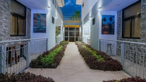 A corridor with a central pathway flanked by railings and greenery, leading to a building entrance with a glass door. - Havana jacó (Jacó)