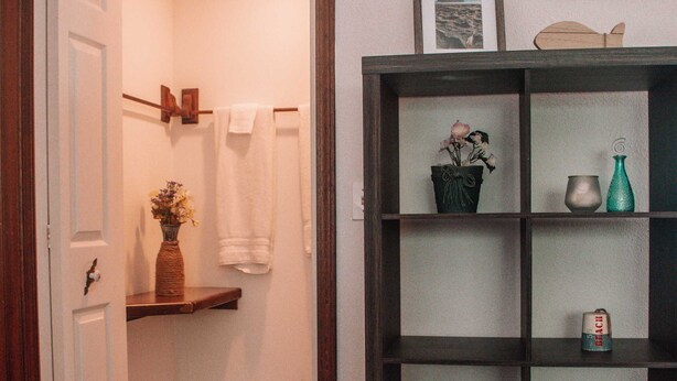A hallway with a wooden door, a small shelf with a vase and towels, and a cabinet with bowls and a can. - Coastal Studio (Brookings)