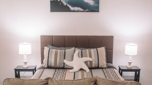 A bedroom with a bed, a nightstand with a lamp, a sofa with cushions, and a wall-mounted picture. - Coastal Studio (Brookings)