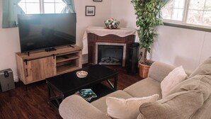 A living room with a flat-screen TV on a wooden stand, a fireplace, a sofa, and a potted plant. - Coastal Studio (Brookings)