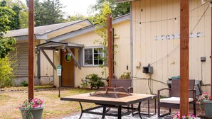 A small guest house with a patio area featuring a table and chairs, surrounded by potted plants and a welcome sign. - Coastal Studio (Brookings)