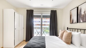 A hotel room with a bed, a wardrobe, a balcony with a table and chairs, and a view of buildings outside.