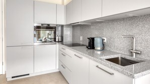 A modern kitchen with white cabinets, a granite countertop, a built-in oven, and a stainless steel sink.