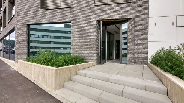 A modern building with a brick facade, large windows, and a set of concrete steps leading to an entrance.