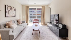 A modern living room with a grey sofa, a round coffee table, a TV, and a large window with curtains.