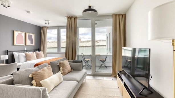 Ett modernt hotellrum med en stor säng, en grå soffa och en tv.