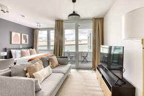 Una habitación de hotel moderna con una cama grande, un sofá gris y un televisor.