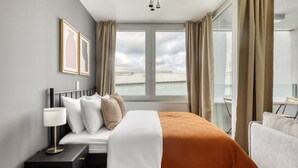 Ett hotellrum med en säng, ett skrivbord, en stol och ett fönster med gardiner.