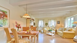 Een ruime woonkamer met een eethoek, met rieten meubels, een houten tafel en een zithoek.