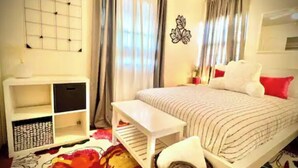 A bedroom with a bed, a bedside table, a chair, a wall-mounted artwork, and a window with curtains.