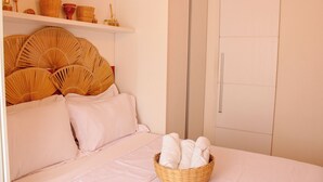 A bedroom with a bed, a wicker basket with towels, and a shelf with baskets and jars. - AxéHome | Charming Accommodation | 2 Bedrooms / 2 Bathrooms (Salvador)