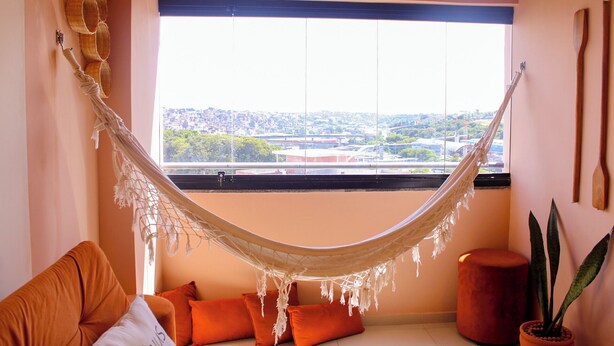 A hammock suspended from a window, a sofa with orange cushions, and a potted plant. - AxéHome | Charming Accommodation | 2 Bedrooms / 2 Bathrooms (Salvador)