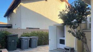 A stone patio with a door, two trash bins, a washing machine, and a small tree. - 2 BD Quiet Neighborhood with AC, Desk, Fast Wifi (Torrance)