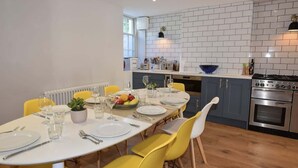 Eine moderne Küche mit weiß gefliester Spritzschutzwand, Edelstahlgeräten und gelben Stühlen um einen Esstisch für vier Personen.